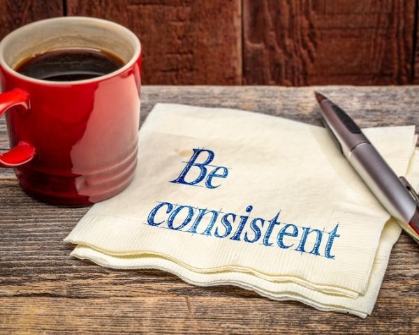 A cup of coffee next to a note saying "Be Consistent".