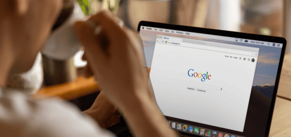 A man sipping coffe next to his laptop about to emobark on some google paid search services.